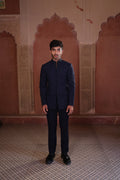 Man in a dark blue jacket and black pants standing in front of ornate pink walls.