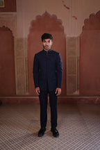 Man in a dark blue jacket and black pants standing in front of ornate pink walls.